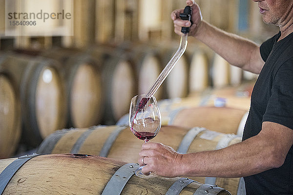 Schrägansicht eines Sommeliers  der mit einer Pipette Wein aus einem Fass ausgießt