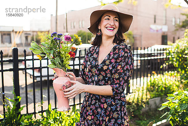 glückliche Frau lächelt im Stadtgarten mit frischen Blumen