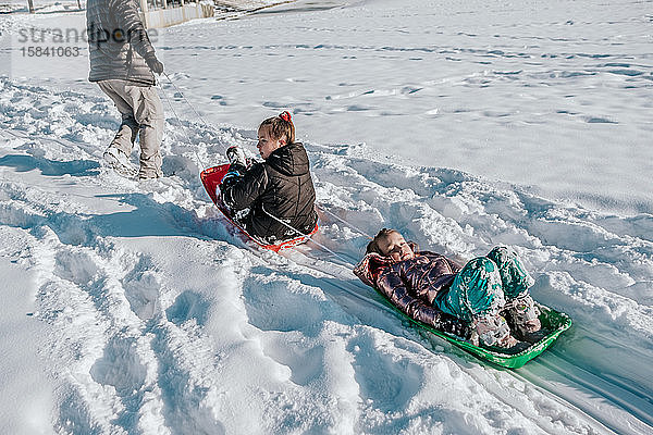 Nach unten schauendes Foto eines Mannes  der im Winter zwei Kinder auf einem Schlitten zieht