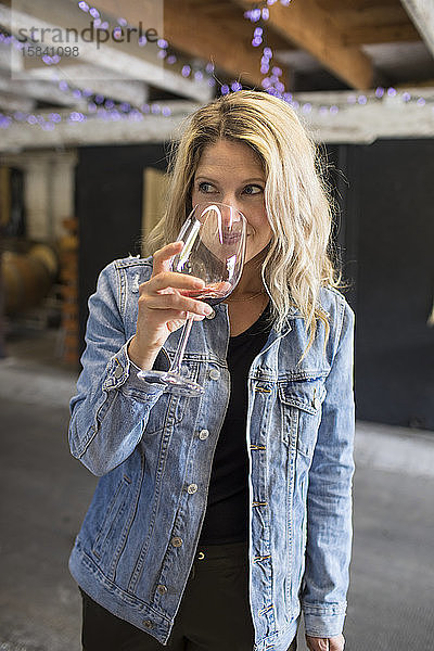 Junge attraktive Frau  die an einem Glas Rotwein auf einem örtlichen Weingut riecht.