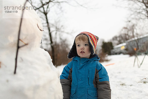 Mittlere Aufnahme eines Kleinkindes mit Strickmütze  das stehend auf einen Schneemann schaut