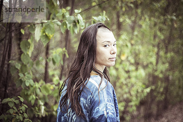 gemischtrassiges asiatisches Mädchen mit rasiertem Ninja-Haar schaut in Bäumen in die Kamera