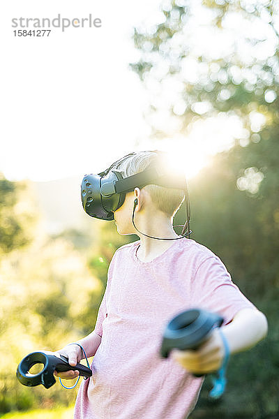 Teenager mit virtueller Erfahrung mit VR-Headset und Reglern im Freien