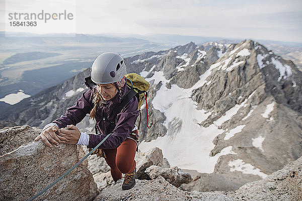 Weibliche Felskletterin mit Helm erklimmt eine Klippe in den Tetons