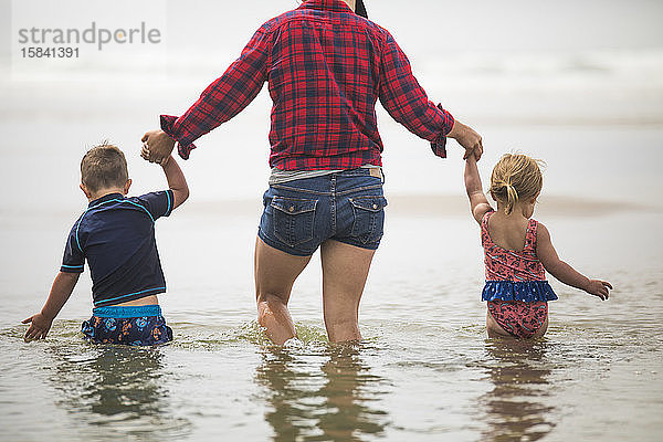 Rückansicht der Mutter  die den Kindern hilft  am Strand durchs Wasser zu waten.