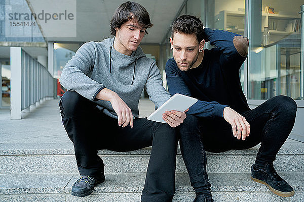 Frontansicht von zwei jungen Männern  die sich unterhalten  auf einer Stadttreppe sitzend und lo