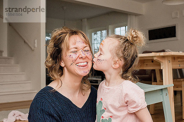Mutter und Tochter spielen zu Hause mit Schminke und lachen zusammen