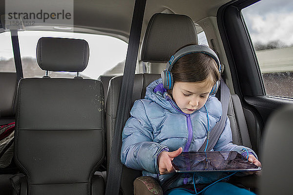 Vorderansicht eines Kleinkindes in einem Autositz  das auf einen Tablet-Bildschirm schaut