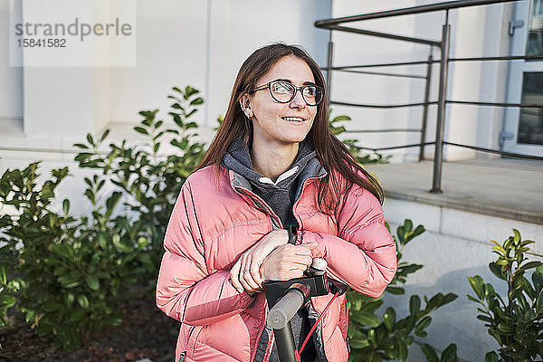 ein tausendjähriges junges Mädchen in einer rosa Jacke auf einem Elektroroller