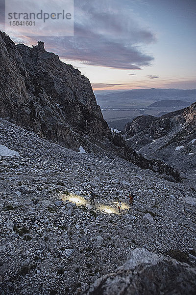 Drei Wanderer mit Scheinwerfern wandern durch die Morgendämmerung in den Tetons