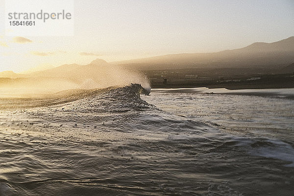 Launische Strandszene einer brechenden Welle mit Uferlinie im Hintergrund