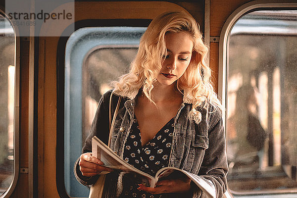 Junge Frau liest Zeitschrift  während sie in der U-Bahn reist
