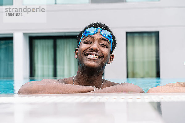 Junger Mann mit Schwimmbrille auf dem Kopf und schnorchelnd am Rand eines Pools lehnend