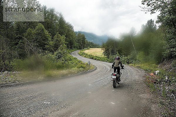 Eine Frau fährt mit ihrem Motorrad auf einer Schotterstraße in Kanada.