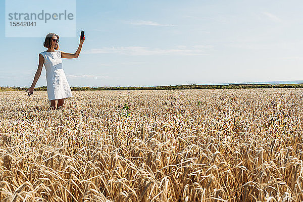 Frau versucht starkes Handysignal im goldenen Feld zu bekommen.