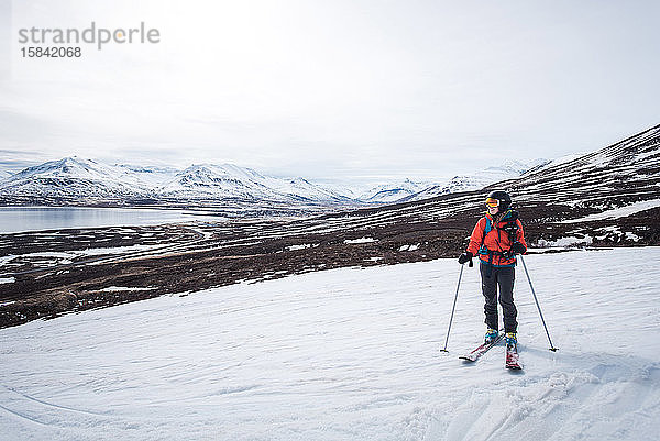 Eine Frau steht mit Skiern auf Schnee mit Bergen und Wasser dahinter