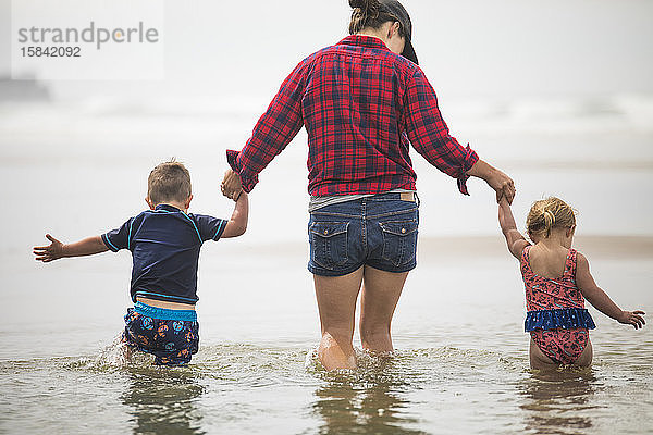 Rückansicht der Mutter  die den Kindern hilft  am Strand durchs Wasser zu waten.