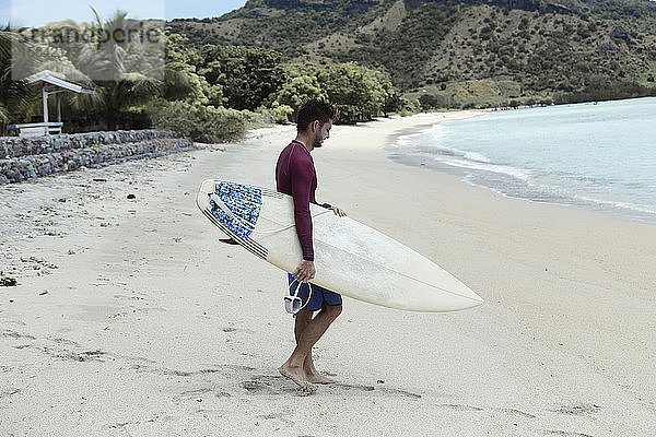 Junger Mann mit Surfbrett am Strand