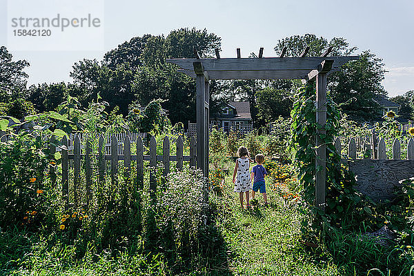Zwei Kinder stehen unter einem Bogen in einem Garten.