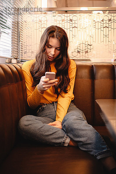 Teenagerin benutzt Smartphone  während sie im Café sitzt