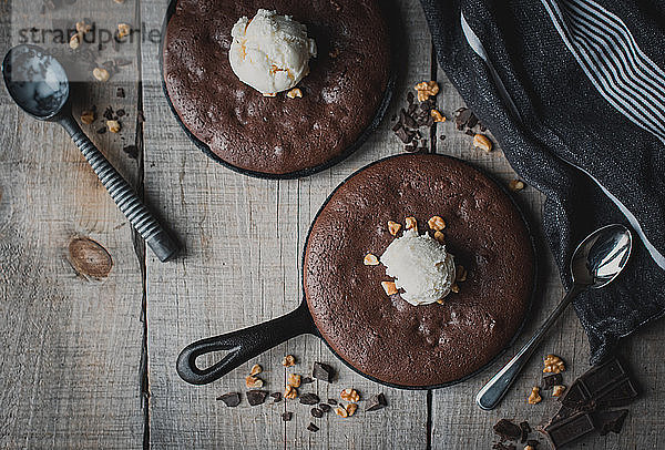 Draufsicht auf Brownies mit Eis und Nüssen in gusseisernen Pfannen.