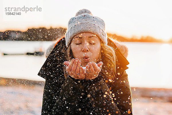 Frau weht goldenen Schnee bei Sonnenuntergang im Winter