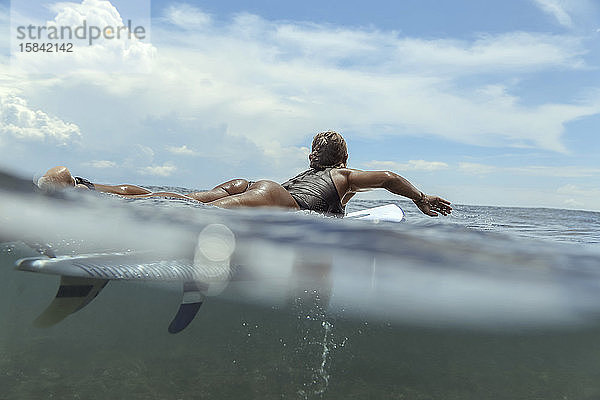 Frau liegt auf einem Surfbrett auf dem Meer