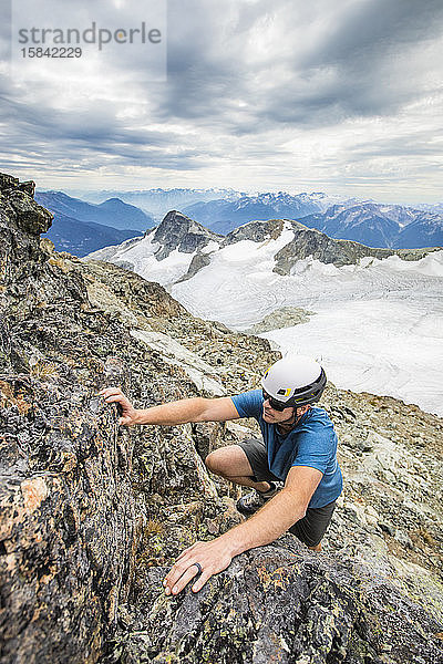 Bergsteiger mit Helm klettert auf den Gipfel eines Berges.