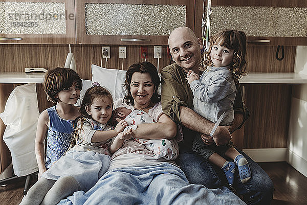Mittelansicht der ganzen Familie  die den neugeborenen Sohn hält und lächelnd im Krankenhaus liegt