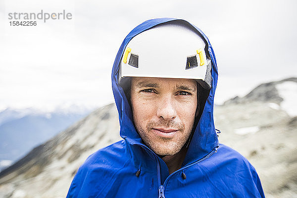 Porträt eines Bergsteigers mit Helm und Regenjacke.