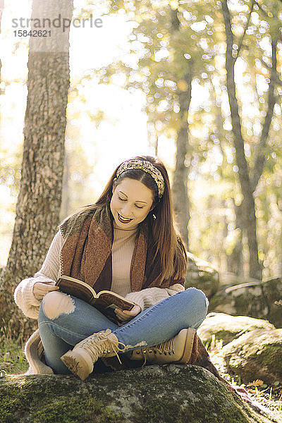 Junge Frau liest sitzend und umgeben von einem Wald ein Buch