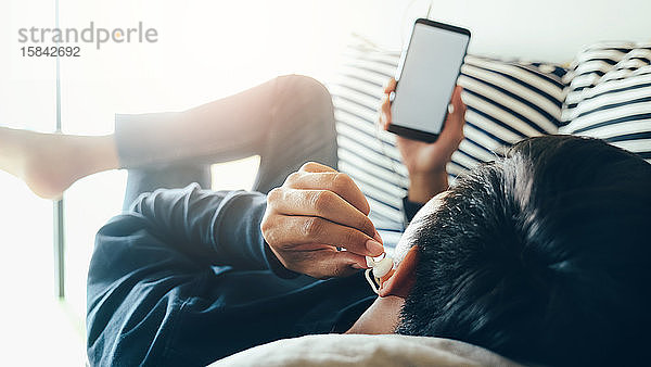 Junger Mann entspannt sich beim Hören der Musik vom Mobiltelefon aus.