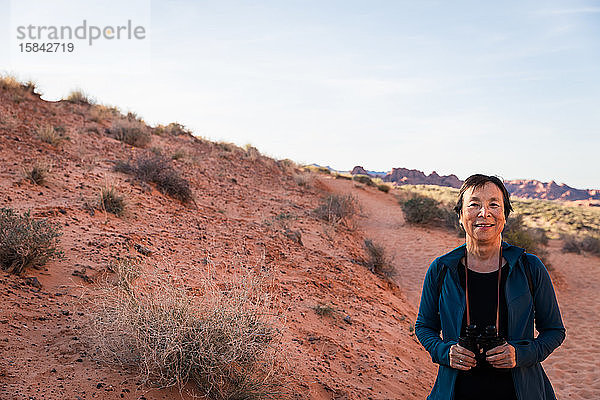 Ältere asiatische Frau lächelt mit Fernglas in der Wüstenlandschaft