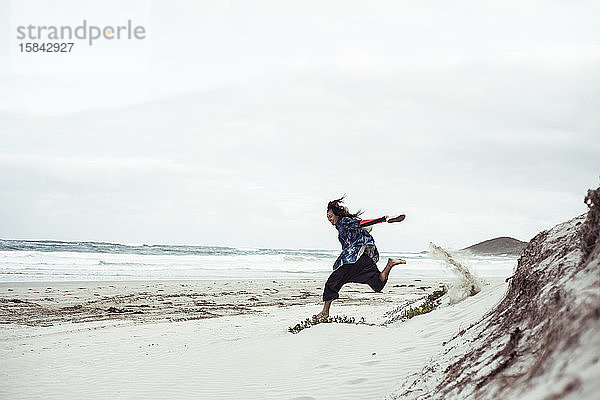 Androgyne Frau rennt und springt von weißer Sanddüne am abgelegenen Strand