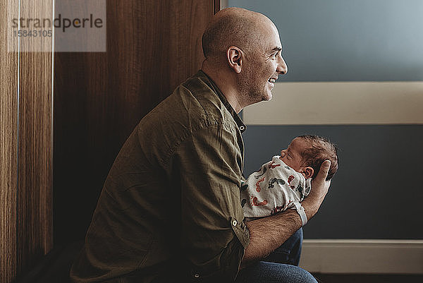 Seitenansicht eines glücklichen Vaters  der seinen neugeborenen Sohn im Krankenhaus hält