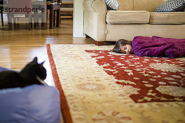 Ein kleines Kind schläft fest schlafend im Schlafsack auf dem Boden mit einer Katze