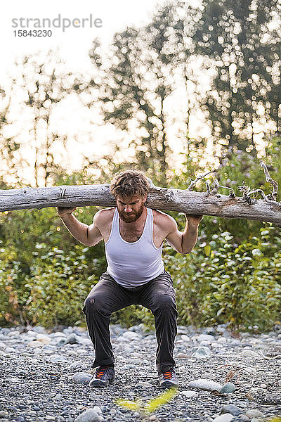 fitter Mann bereitet sich darauf vor  während eines Trainings im Freien einen Baumstamm zu schultern.