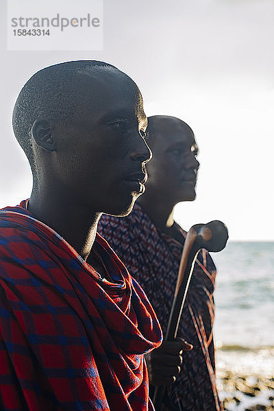 Zwei Massai-Männer in traditioneller Kleidung stehen vor dem Meer