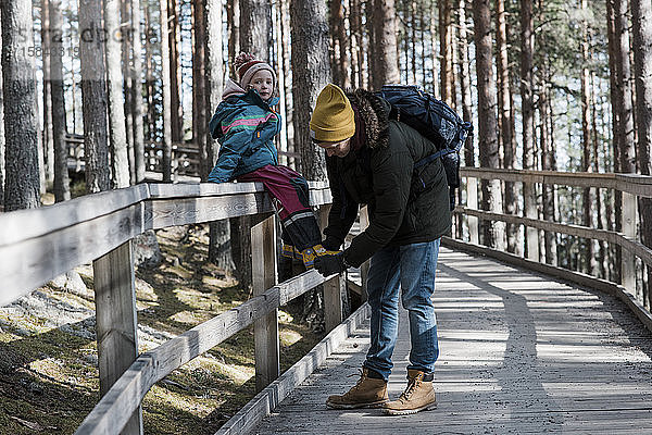 der Vater hilft seiner Tochter beim Schuhanziehen  während sie im Wald spazieren geht