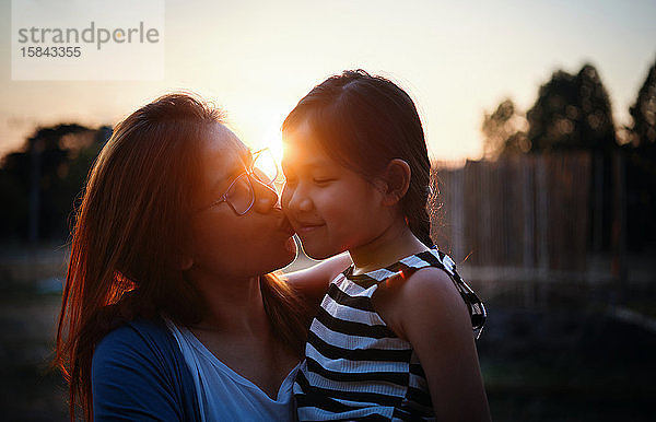 Mutter küsst ihre Tochter bei Sonnenuntergang