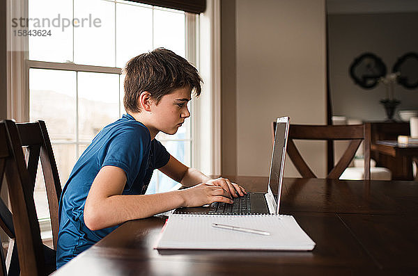 Zwischenmensch  der zu Hause auf einem Laptop an seinen Hausaufgaben arbeitet.