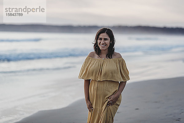 Lifestyle-Porträt einer jungen Frau  die am Strand vor bewölktem Himmel spazieren geht