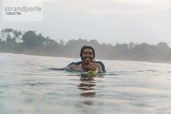 Porträt eines glücklichen Mannes  der auf einem Surfbrett auf dem Meer liegt