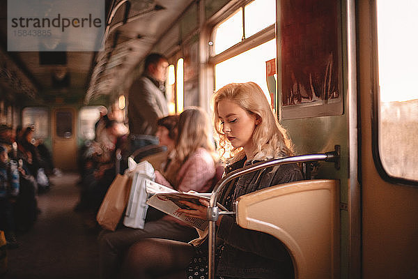 Junge Frau liest Zeitschrift  während sie in der U-Bahn reist