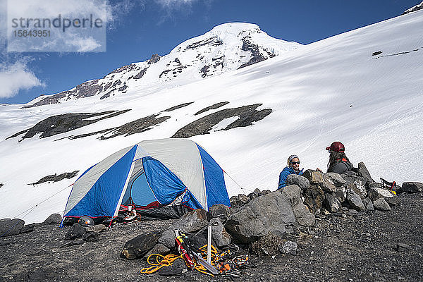 Zwei Bergsteigerinnen sitzen sprechend neben dem Zelt auf dem Mount Baker