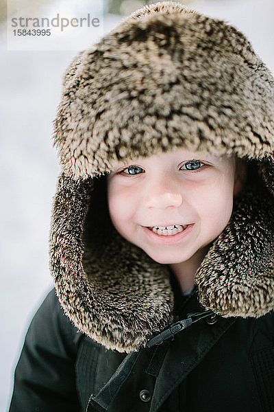 Nahaufnahme Kleinkind Junge lächelt mit Pelzmütze im Schnee