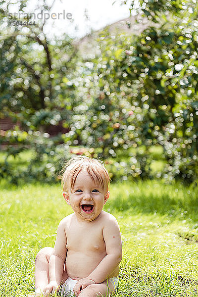 Kleiner Junge sitzt auf dem Rasen und lacht