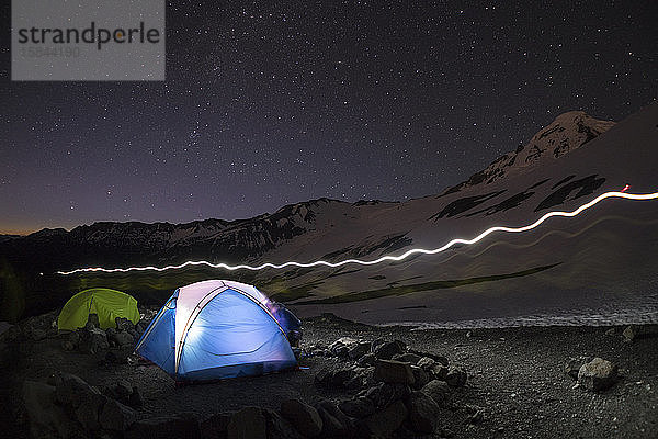 Ein Licht leuchtet aus einem blauen Zelt  während über dem Basislager Mt. Baker Sterne leuchten