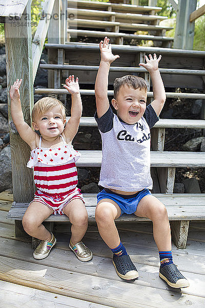 Zwei glückliche Kinder  die auf einer Treppe sitzen  heben zur Feier die Hände.
