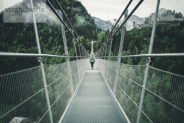 Junge Frau wandert über Hängeseilbrücke in alpiner Umgebung